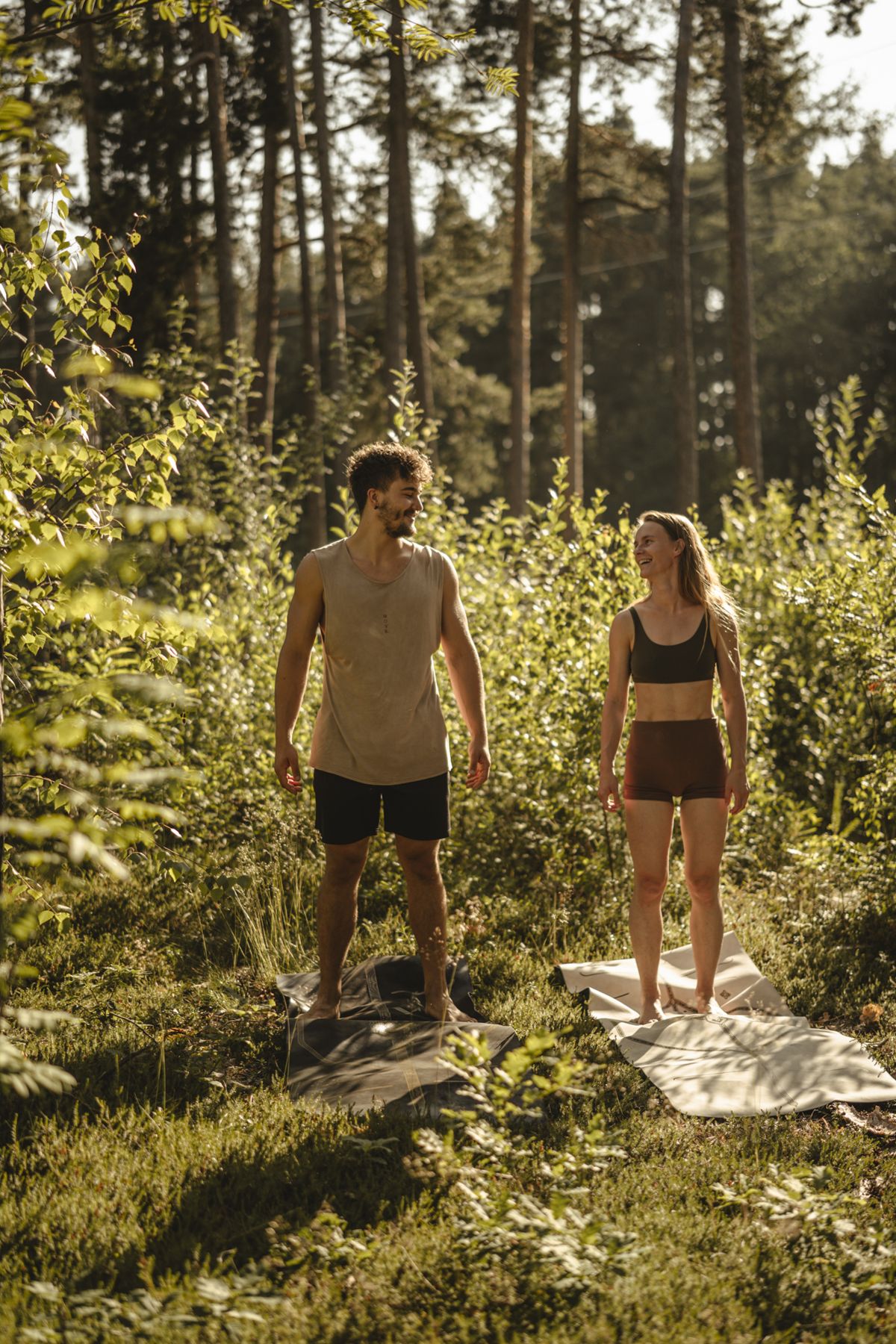Martin und Steffi lachend auf ihren Yogamatten im sonnigen Wald