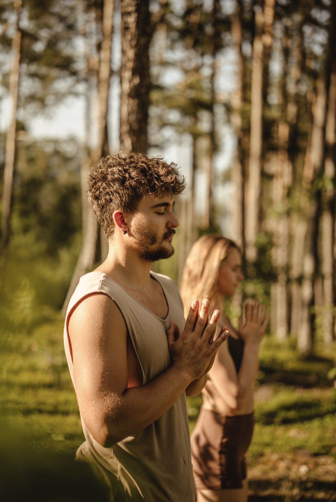 Martin und Steffi mit Händen vor dem Herzen bei einer Yogaeinheit im Wald