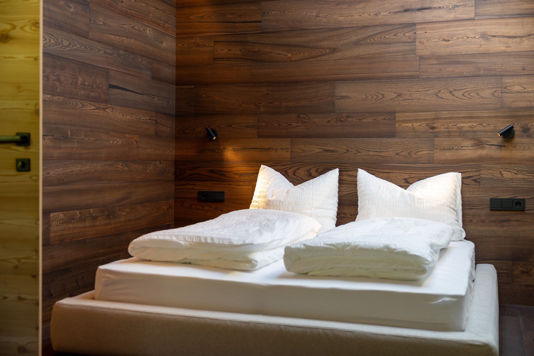 Schlafzimmer mit weißem Bett vor dunkler Holzwand
