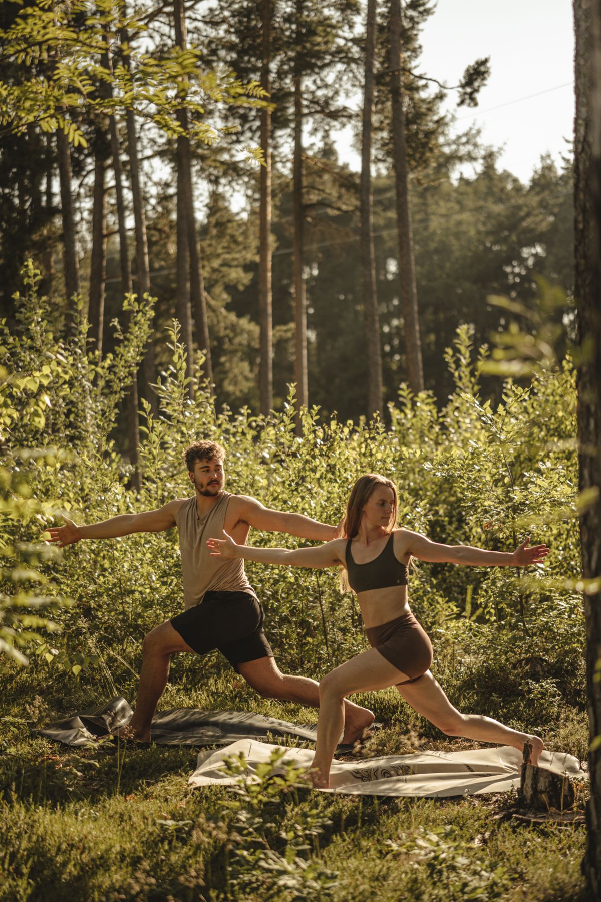 Martin und Steffi im Krieger II auf ihren Matten im sonnigen Wald